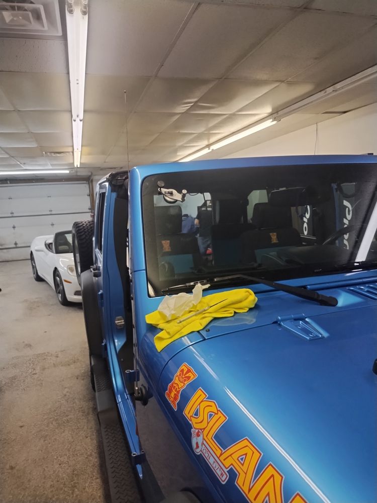 Blue Jeep Wrangler inside a garage with repair tools and a yellow cloth on the hood