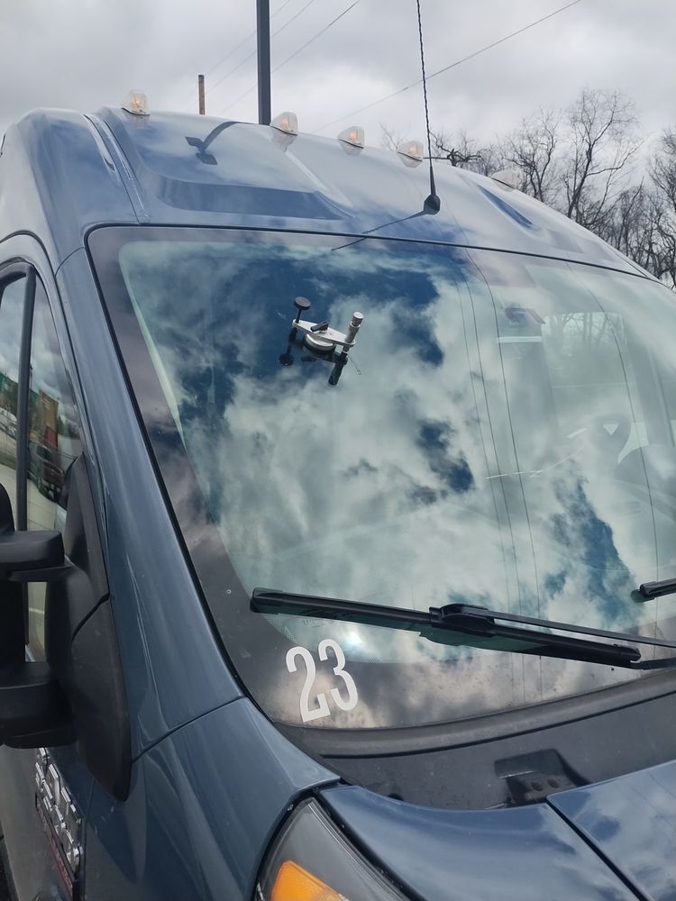 Repair bridge on the windshield of a grey fleet van numbered 23, clouds reflected in the glass
