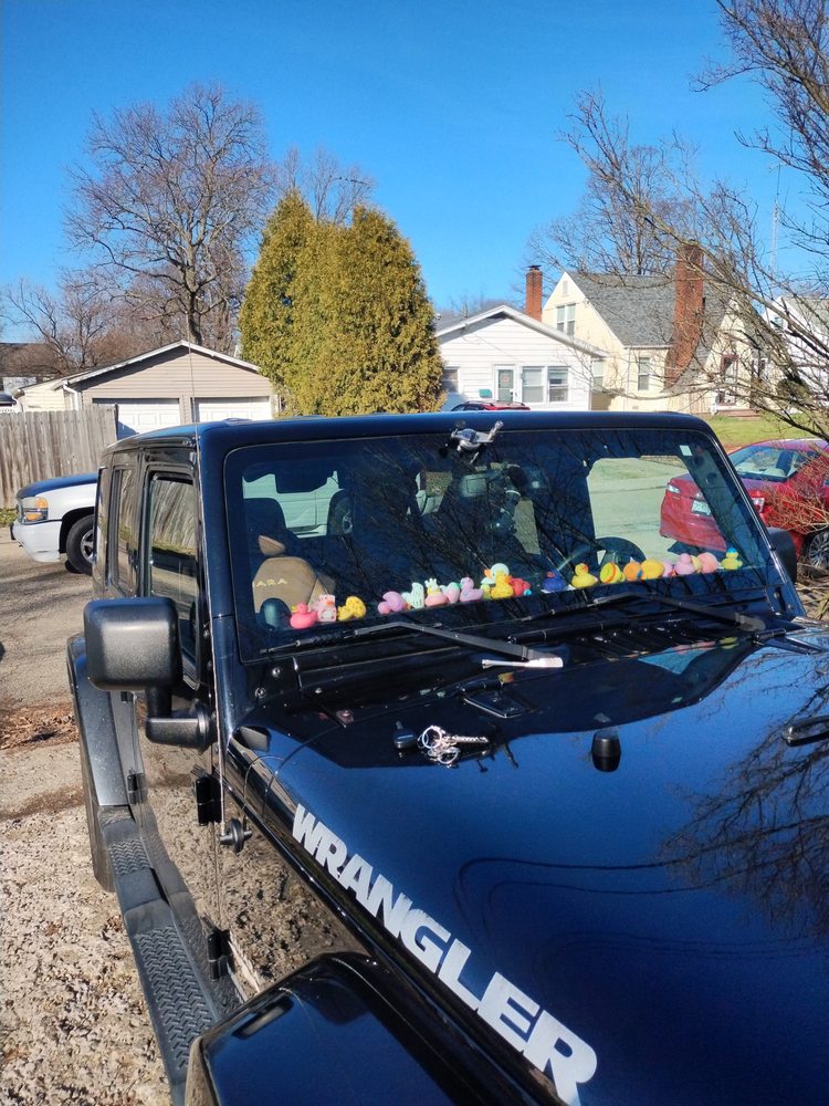 Dark blue Jeep Wrangler in a driveway, repair tool on the windshield and rubber ducks along the dashboard